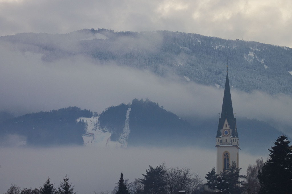 Weltcup-Strecke im dichten Nebelband und St. Andrä Kirchturm
